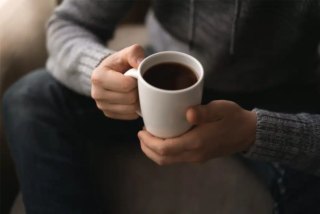 Close-up of hands holding a white mug, highlighting caffeine's role in rhinoplasty recovery.