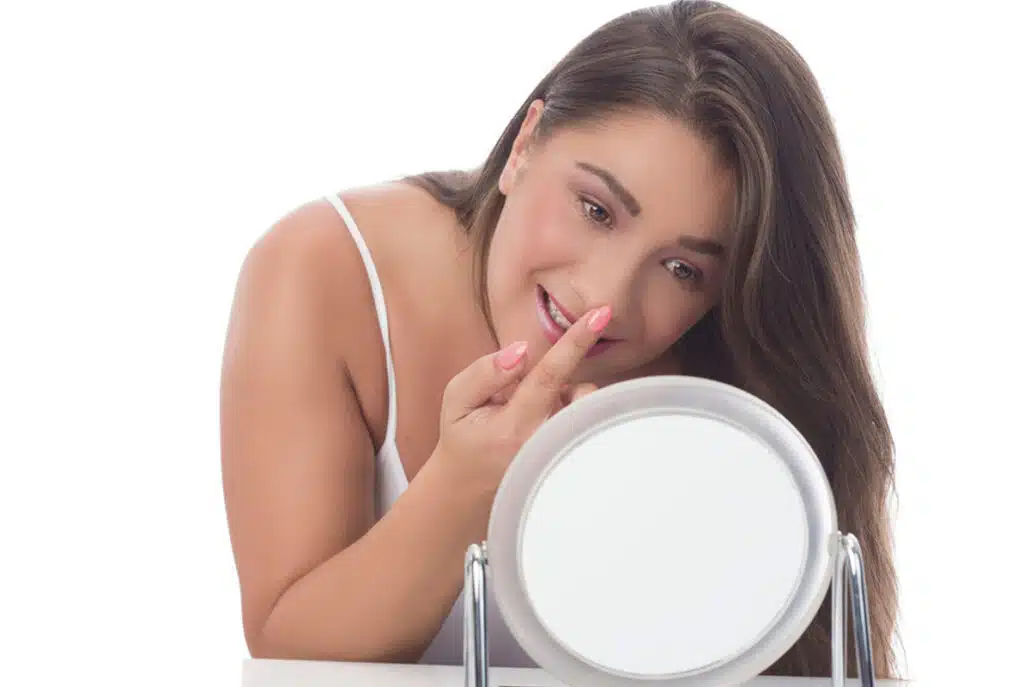 Woman checking nose in the mirror for post-operative changes