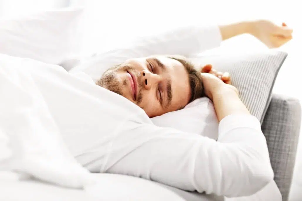 Man sleeping peacefully on white bedding, representing improved breathing and rest after septorhinoplasty recovery.
