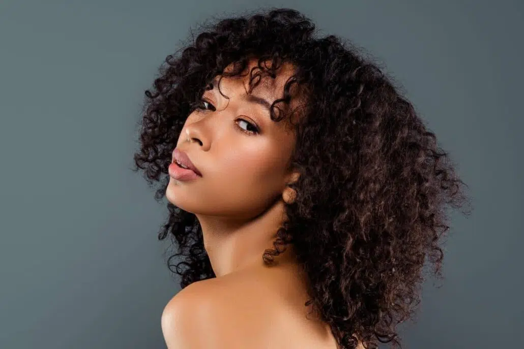 Confident woman with curly hair and defined nose, representing ideal ethnic rhinoplasty candidate seeking subtle results